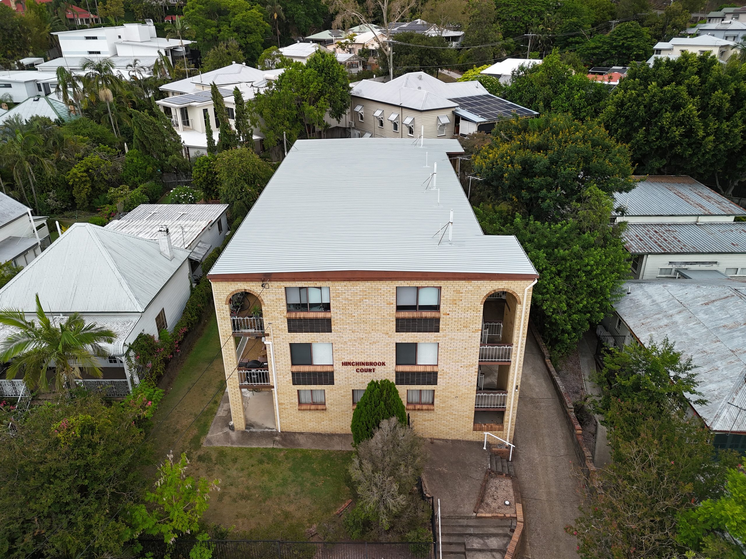 Aerial view of a three-storey brick apartment building named Hinchinbrook Court, surrounded by established trees in the Brisbane suburb of Kelvin Grove.