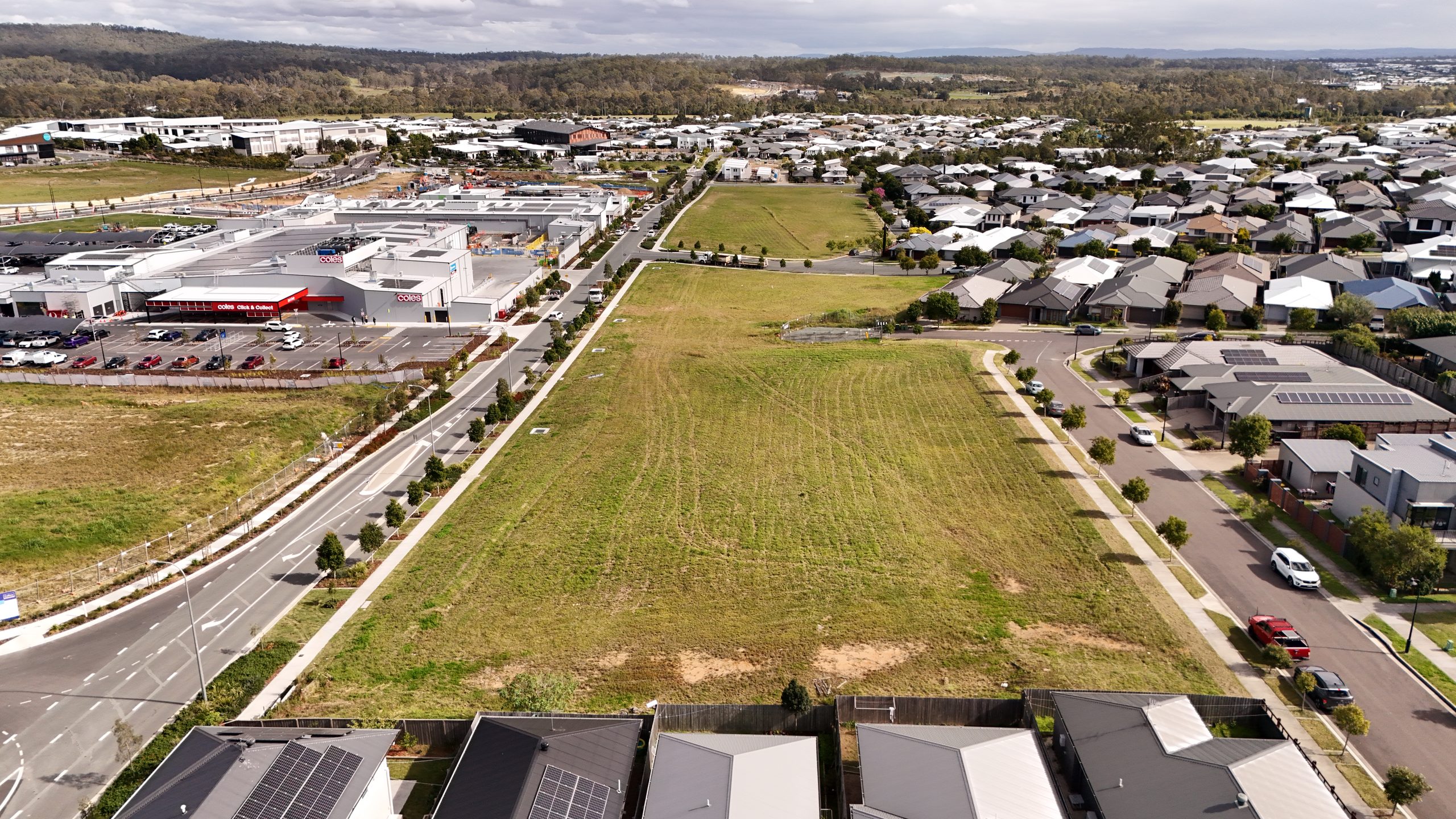 Aerial view of a residential housing estate adjoining a shopping centre with a Coles supermarket, car park and surrounding streets.