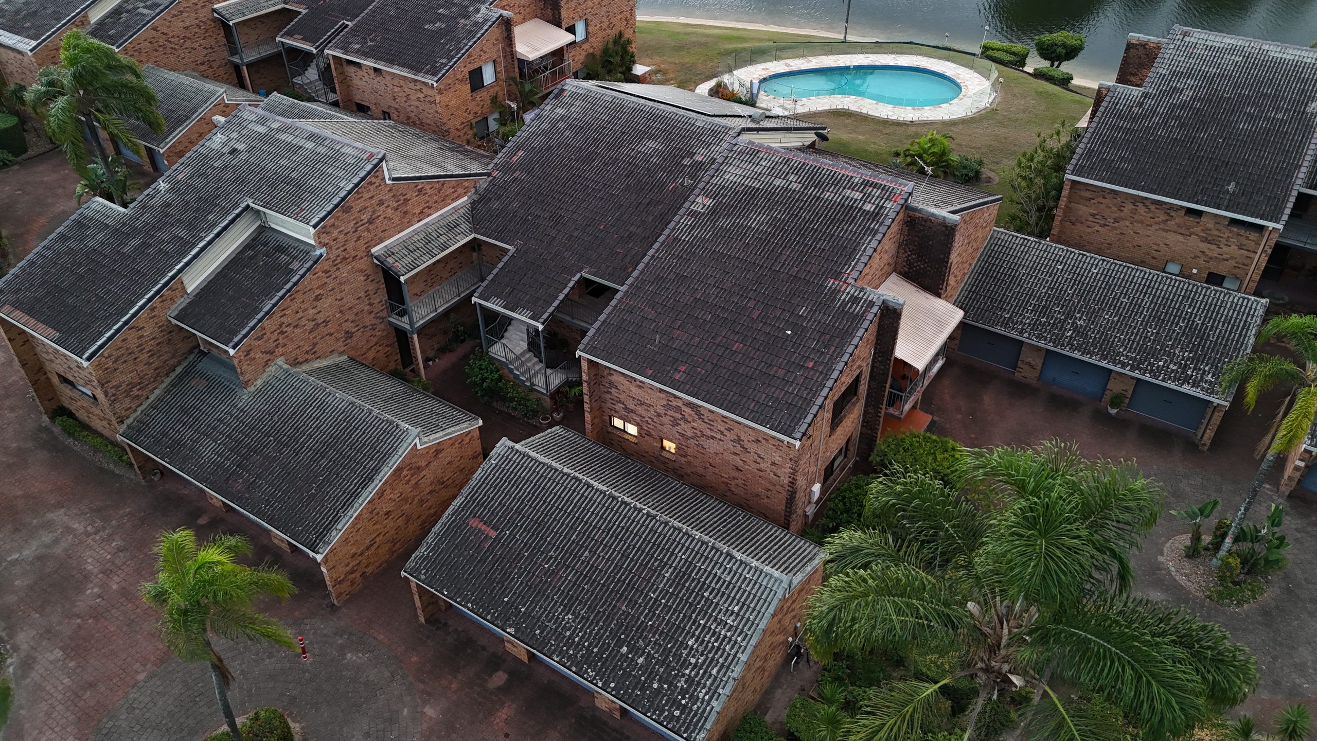 Daytime aerial view of a large home with a swimming pool, curved driveway and established gardens in Mermaid Waters, Queensland.