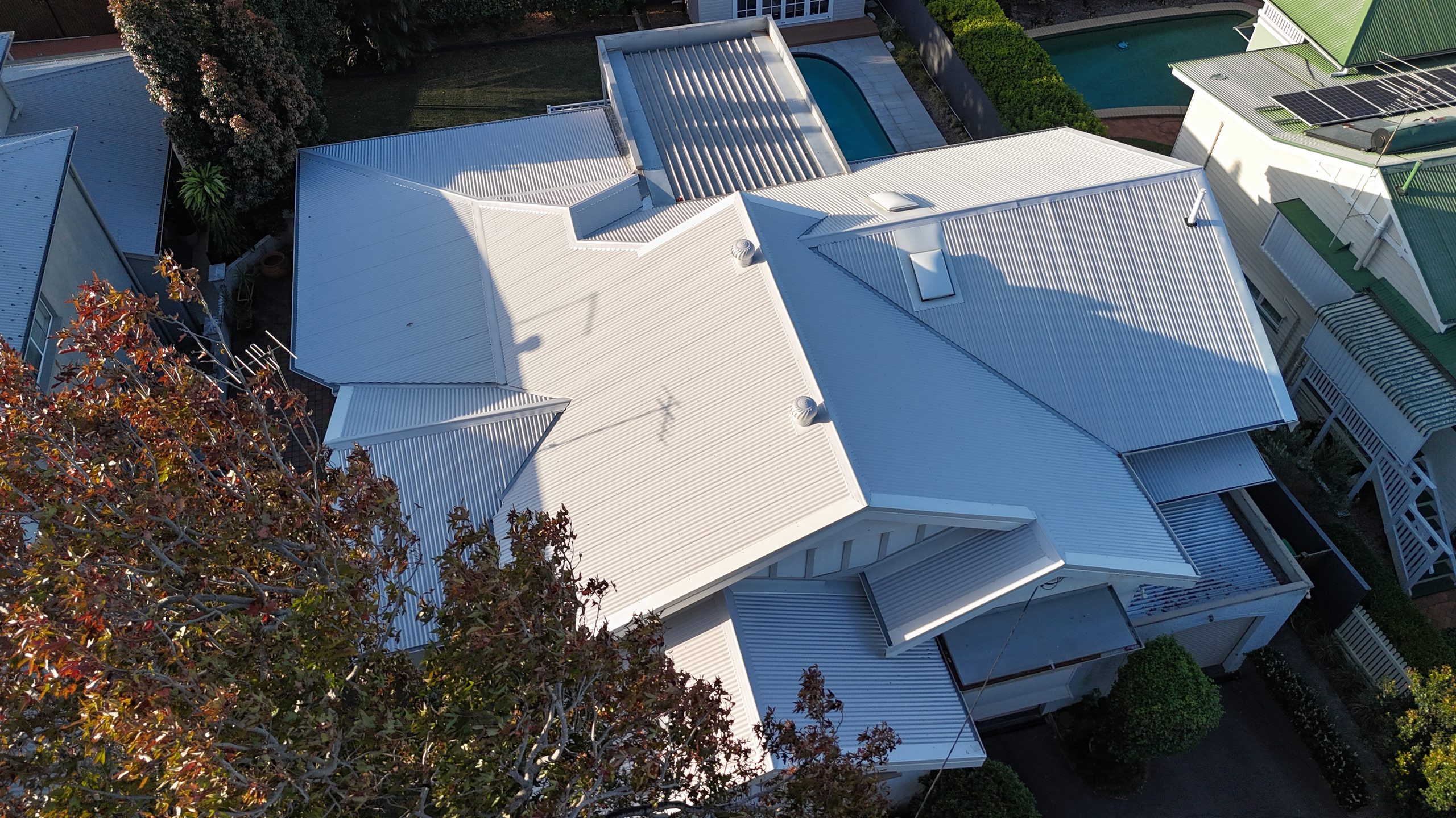 Aerial view of a house with a newly installed white metal roof, pool and garden in Ascot, Brisbane, in warm afternoon light.