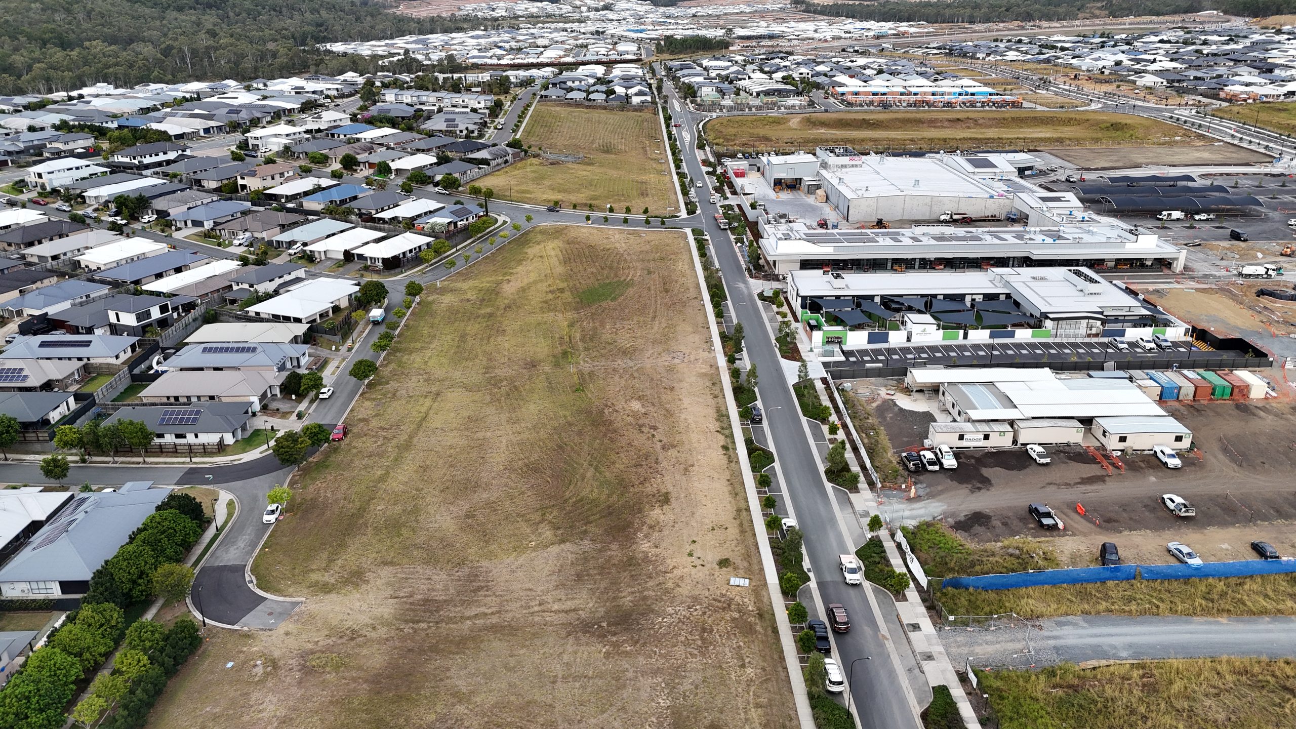 Aerial view of a vacant development lot beside new homes and a partially built shopping centre in a Brisbane growth corridor.